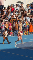 Children perform dance routine on outdoor court for seated audience