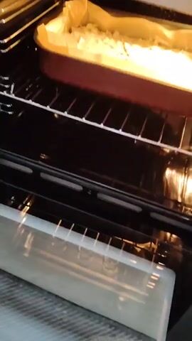 The video shows an open oven with a pan of food on the rack. The food appears to be in the process of baking, with a golden-brown crust. The oven light is on, illuminating the interior. The camera pans across the oven, providing a close-up view of the food. The scene is domestic and appears to be a kitchen.