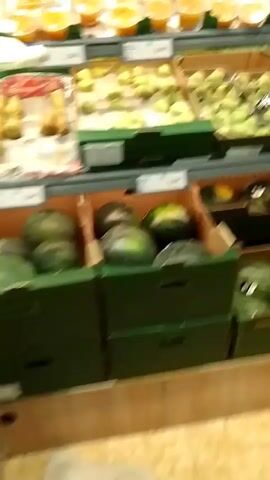 The media file captures a scene in a grocery store, likely a produce section, in Aspropyrgos, Greece. The camera pans across various displays of fruits and vegetables. In the foreground, there are boxes filled with watermelons and what appear to be pears or apples. Further back, shelves are stocked with bottled beverages, including juices. A digital scale is visible on a counter, suggesting customers can weigh their produce.

The lighting suggests it is daytime, and there are no indications of weather conditions. The overall atmosphere seems to be that of a typical shopping environment, with no particular emotional tone conveyed. The focus is on the merchandise and the layout of the store.

Some text is partially visible on price tags and labels on the shelves, but it is too blurred to be legible. The presence of crates and the arrangement of produce suggest a retail setting where goods are presented for sale. A person is partially visible in the background, wearing a blue shirt and dark pants, and another person with dark leggings and a patterned top, but their actions are not clear. The flooring appears to be tiled.