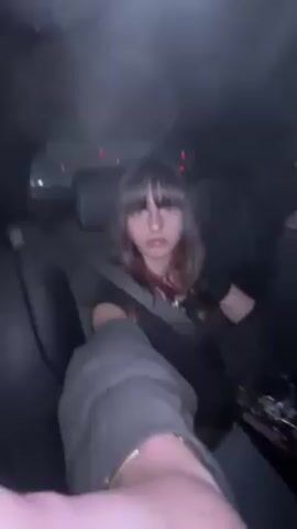 A person is in the back seat of a car. The person appears to be filming a selfie video. The camera pans around to show a person in the front seat driving. The scene appears to be a nighttime city street.
