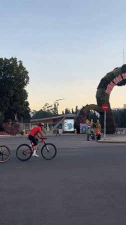 Cyclists in red ride through flower archway in Da Lat
