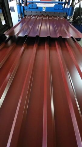 The video shows a close-up, static shot of corrugated red metal sheets. The sheets have raised parallel ridges running lengthwise. They are positioned one above the other, with the top sheet slightly offset to reveal the ridge pattern.  The metal is shiny and reflects light. In the background at the top of the frame, a blue machine is visible, appearing to be part of a manufacturing process.