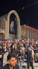 Nighttime crowd rally in Tehran with red flags and phone lights