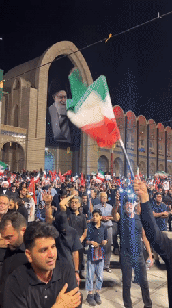 Nighttime crowd rally in Tehran with red flags and phone lights