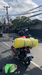 Motorcyclist carries large yellow cylinder through Denpasar streets