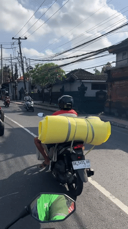 Motorcyclist carries large yellow cylinder through Denpasar streets