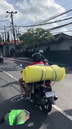 Motorcyclist carries large yellow cylinder through Denpasar streets