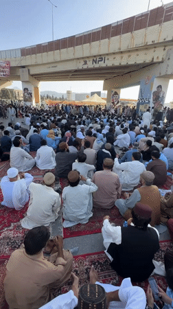 Outdoor prayer gathering on red carpets beneath Quetta overpass