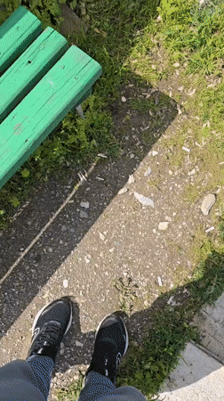 Person filmed standing on gravel path near green bench