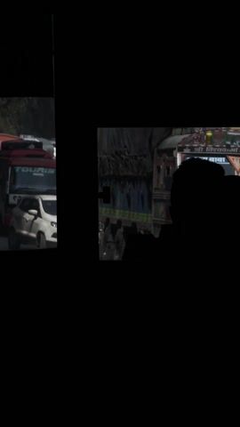 The video shows traffic congestion on a dusty road. On the left, a gray SUV moves towards the camera, kicking up dust. Various vehicles, including a "TOURIST" van, a white truck, and several cars, are seen in the right side of the frame, interspersed by a blacked-out silhouette. The congestion implies a slow-moving or stationary traffic situation.