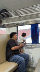 Father shows baby train window view in Indonesia