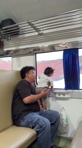 Father shows baby train window view in Indonesia