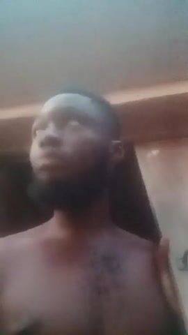 A shirtless, dark-skinned man with a beard looks around a car.