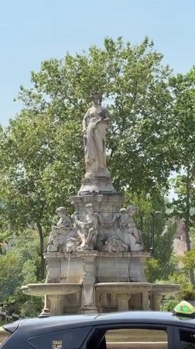 Taxi parked by fountain in Lyon under sunny skies