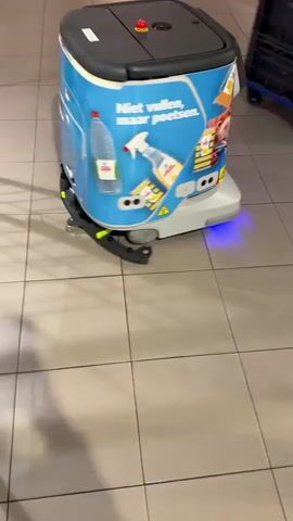 The video begins with a shot of a cleaning robot with the text "Niet vullen, maar poetsen" and cartoon images of cleaning supplies and a hamster. The robot has a screen displaying "00" and a blue light at its base. As the video progresses, the robot moves, and the screen displays "00" with animated eyes. The surrounding environment appears to be a tiled floor in what looks like a store or supermarket, with shopping carts and a person wearing jeans and white sneakers visible in the background. The robot continues to move, and its blue base light is visible. At the end of the video, the base light changes to red.