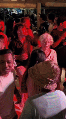 Multi-generational crowd dances at thatched-roof bar during afternoon