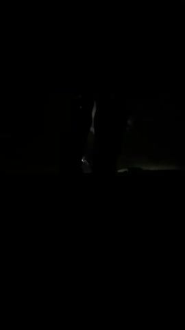 The video shows a person's face formed by what appears to be condensation or fog on a windshield at night. The face has two large, dark eye-like shapes and a wider, lighter area below them. The background is black, with faint lights visible in the distance, suggesting the person is inside a vehicle. The lighting shifts, causing the face to appear and disappear in the darkness.