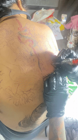 Tattoo artist works on client's back piece in Kuta