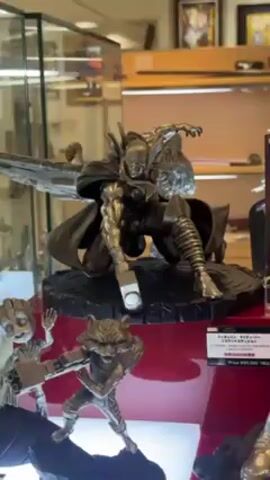 The video shows a display of Marvel character statues. The statues include Thor, Rocket Raccoon, Thanos, and Spider-Man. The statues are primarily metallic bronze or gold in color. They are displayed on a red base in a well-lit store with various framed pictures and other items visible in the background.  A person wearing a mask walks by in the background.