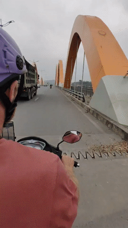 Scooter rider crosses bridge in Vietnam under overcast skies
