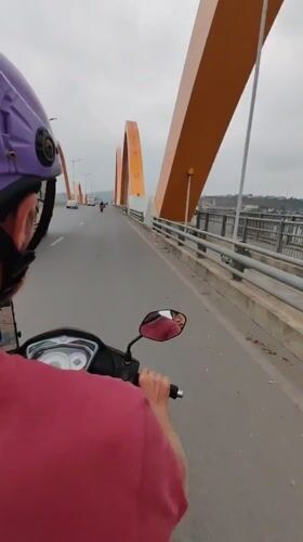 Scooter rider crosses bridge in Vietnam under overcast skies