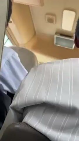The video is taken from inside a moving vehicle, focusing on the back of the heads of two people. The person in the foreground is wearing a gray and white striped shirt and has short, dark hair. The person to their left is wearing a white shirt and black pants. The interior of the vehicle is beige, and there are vents and lights visible on the ceiling. The camera is steady, and the focus is on the clothing of the people.
