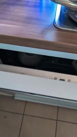 The video shows the inside of a dishwasher filled with dirty dishes. The dishwasher is a stainless steel appliance and appears to be in a home kitchen. The dishes include plates, bowls, glasses, and cutlery. Some of the dishes are stacked, while others are placed loosely in the racks. There is also a pot with a black, textured bottom on the lower rack. A pink utensil is visible in the cutlery basket. The lighting suggests it is daytime. No people are visible in the video. The location context of Harsewinkel, Germany, is provided but not visually evident in the footage. There is no visible text.