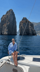 Woman sails near Capri's Faraglioni rocks under clear skies