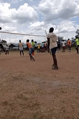 Young adults play volleyball on dirt court in Kenya