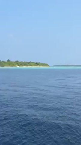 The video shows a view of the ocean with two islands in the distance. The water is deep blue and slightly choppy. The islands appear to have sandy beaches and are covered in lush green vegetation. The sky is clear and light blue.