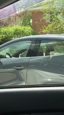 The video, shot from within a car, shows a drive through a residential area. The driver's side window frames the view of houses with well-maintained lawns and sidewalks. 

The opening shot reveals a woman walking on the sidewalk, engrossed in a phone conversation while carrying a pink duffel bag. The camera then captures various houses as the car moves. One house is yellow with a red door and porch stairs. Another is blue with a green door, showcasing a small porch and landscaped greenery. Several parked cars are visible along the street. The weather appears sunny. The overall tone suggests a leisurely drive through a quiet, suburban neighborhood.