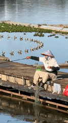 Masked fisherman in conical hat casts from Da Lat pier