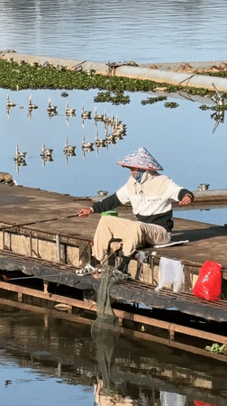 Masked fisherman in conical hat casts from Da Lat pier