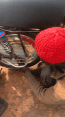 Person performs motorcycle maintenance on dirt ground outdoors