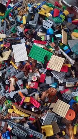 This media file is a close-up, top-down shot of a large pile of Lego bricks. The bricks are a mix of colors and shapes, including standard bricks, plates, and some specialized pieces like wheels and figures. Some of the figures appear to be Lego minifigures. The pile is densely packed, with some bricks partially obscuring others.

There are no discernable people in the media file, although a hand briefly enters the frame in the first and last segments, suggesting a person is interacting with the Lego pile. The lighting is bright and even, indicating an indoor setting, possibly a room with good overhead lighting. There are no clear weather or time of day cues. The environment appears to be a typical home or play area, with the Lego bricks scattered on a wooden surface, likely a floor or table.

The activity taking place is simply the presence of a large collection of Lego bricks. There are no specific building projects or actions depicted beyond the initial brief interaction with the pile. The overall mood conveyed is one of potential for play and creativity, as is typical with Lego. There is no visible text within the media file. The context provided suggests the location is Vrútky, Slovakia, but this is not visually evident within the media itself.