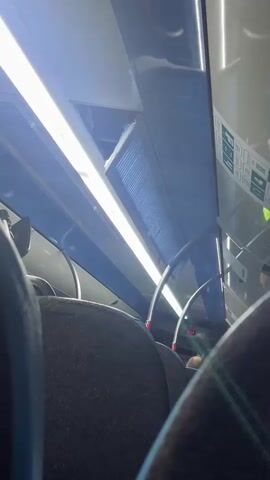 The video shows the interior of a public transport vehicle, likely a bus or train, in Telde, Spain. The camera is positioned behind two seats, looking forward and slightly upwards towards the ceiling. Overhead, bright, linear LED lights illuminate the cabin. Blue and white panels line the ceiling, with one panel appearing slightly open or detached on the left side, revealing a dark cavity above. Air vents are visible along the ceiling.

In the foreground, the backs of dark grey, fabric-covered seats are visible, with blue accents on the side of one seat. Beyond the seats, a small digital display shows "2:03", possibly indicating time or temperature. Safety information placards are affixed to the wall on the right side, though the text is not legible. The vehicle appears to be in motion, suggested by subtle vibrations. No specific human faces or activities are clearly visible, only the presence of passengers implied by the seats and a glimpse of legs/laps.