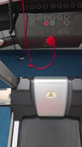 A first-person perspective video shows a person's left leg and foot, wearing a bright green athletic shoe and a gray sock, stepping onto the moving belt of a black and silver treadmill. The treadmill's console is visible above the belt, featuring a red emergency stop clip attached to a red cord. The background is a blue carpeted floor and a white wall. The person is actively walking or running on the treadmill, indicated by the movement of their leg and the belt.