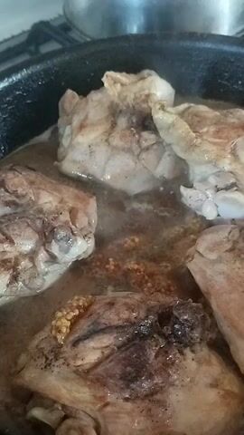 This is a close-up video clip of chicken pieces being cooked in a pan. The chicken is a light brown color, with some darker, seared areas. It is submerged in a liquid, likely a broth or sauce, which is bubbling, indicating it is hot. Several pieces of chicken are visible, some with skin on. The pan appears to be black and is likely cast iron due to its texture. The background shows a stovetop, suggesting the cooking is taking place in a kitchen. There are no people visible in the video. The lighting suggests it could be daytime, but no specific time of day can be determined. There are no visible text elements in the video. The scene is a domestic cooking setting.