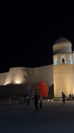 Evening gathering at illuminated Khiva fortress draws visitors and diners