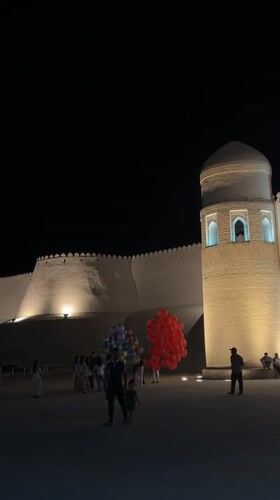 Evening gathering at illuminated Khiva fortress draws visitors and diners