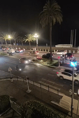 Wet coastal street at night, traffic and pedestrians at a crosswalk