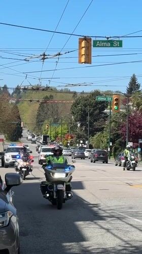 Police motorcade with flashing lights travels through downtown Vancouver