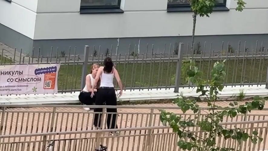 Two people hang out near a fence outside a Khimki building