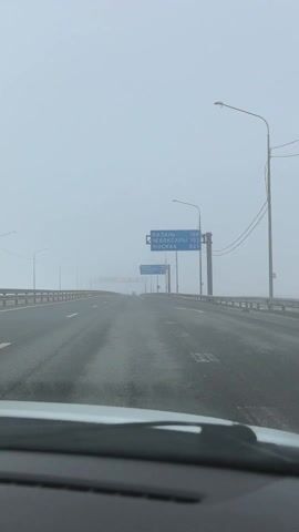 A car is driving down a highway in dense fog. Road signs indicate the distance to Kazan, Cheboksary, and Moscow in kilometers. The road has multiple lanes in each direction and is mostly empty of other traffic. Streetlights line the sides of the highway.