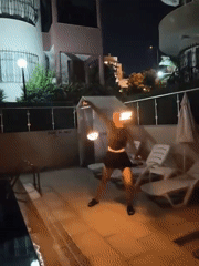 Fire dancer spins flaming poi poolside in Kuşadası at night