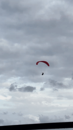 Red paraglider spotted against overcast sky