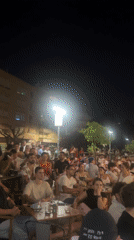 Packed outdoor bar in Palma watches a soccer match at night