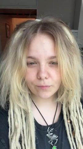 The video shows a close-up of a person with blonde hair and dreadlocks. The person is smiling and their hair is moving. The background is blurry and appears to be indoors.