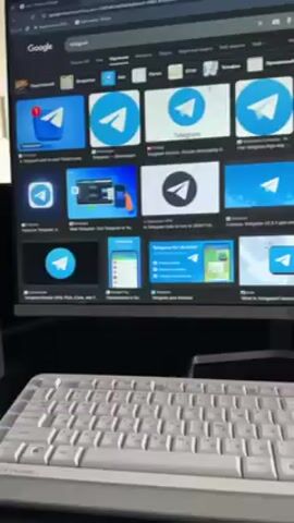 A close-up shot shows a computer monitor displaying an image search for "Telegram" with numerous results of the Telegram logo and related images. In front of the monitor is a white keyboard. The setting appears to be indoors, on a desk. Loud voices can be heard in the background.