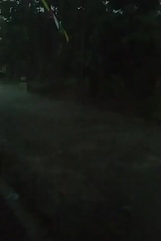 The video shows a dark, misty environment, likely outdoors, with what appears to be water flowing or mist present. The lighting is dim, making details difficult to discern. On the left side of the frame, there are hints of green foliage. A splash of red and yellow is visible in the lower left corner, possibly part of an object or clothing. The overall impression is one of a natural setting, perhaps a forest or a waterfall, shrouded in low light and mist.